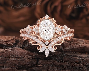 May include: A rose gold engagement ring set with a large oval-shaped center stone and smaller accent stones. The ring features a delicate floral design and a matching band with pearl accents.