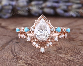 Puede incluir: Un juego de anillos de compromiso de oro rosa con una piedra central de diamante en forma de pera. El anillo está adornado con pequeños diamantes y cuentas turquesas. El juego incluye una banda a juego con cuentas turquesas.