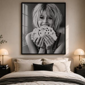 K&ouml;nnte beinhalten: Ein schwarz-wei&szlig; gerahmter Wandkunstdruck, der das Portr&auml;t einer l&auml;chelnden Person mit kurzem Haar zeigt, die einen F&auml;cher aus Spielkarten vor das Gesicht h&auml;lt. Das Bild f&auml;ngt einen nat&uuml;rlichen Ausdruck ein, wobei die Karten das Kinn verdecken.