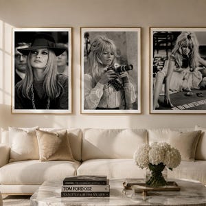 Op de afbeelding: Set van drie ingelijste zwart-witfoto's. De foto's tonen een vrouw in verschillende poses, waaronder een met een camera, een met een hoed en een zittend aan een tafel. De lijsten zijn lichtbruin en de afbeeldingen worden boven een cr&egrave;mekleurige bank weergegeven.