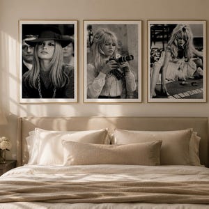 Op de afbeelding: Drie ingelijste zwart-witfoto's van een vrouw worden boven een bed getoond. De foto's tonen dezelfde vrouw in verschillende poses, waaronder een met een camera en een andere die kaarten speelt. De frames zijn goudkleurig.
