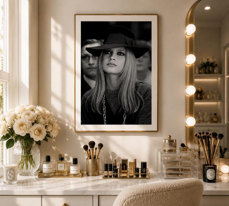 Op de afbeelding: Zwart-witfoto in een lijst van een vrouw met een hoed, met een man op de achtergrond. De foto wordt tentoongesteld boven een kaptafel met make-up en accessoires. Een boeket witte rozen staat in een glazen vaas.