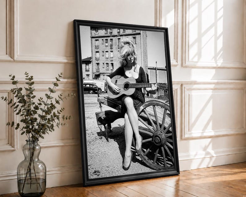 Pu&ograve; includere: Una stampa artistica incorniciata in bianco e nero che ritrae una persona con i capelli lunghi seduta su una ruota di carro in legno mentre suona una chitarra acustica. La scena include un edificio a pi&ugrave; piani sullo sfondo e un'auto parcheggiata.