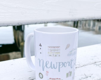 May include: White ceramic mug with a blue and white illustration of Newport, Rhode Island landmarks. The mug has a handle and says "Newport" in blue cursive lettering.