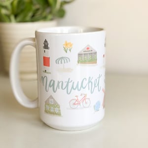 May include: White ceramic mug featuring the word "Nantucket" in a teal script, along with watercolor illustrations of a lighthouse, flowers, a beach umbrella, a bicycle, and other island elements. The mug has a large handle and is filled with a white liquid.