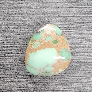 May include: A green and brown variscite cabochon with a teardrop shape. The stone has a mottled pattern of green and brown.