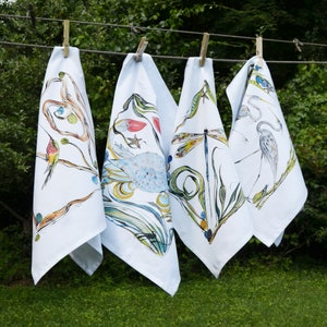 K&ouml;nnte beinhalten: Vier wei&szlig;e Geschirrt&uuml;cher mit farbenfrohen, von der Natur inspirierten Designs. Jedes Handtuch zeigt ein anderes Vogel-, Libellen- und Blumenmuster. Die Handt&uuml;cher h&auml;ngen an einer W&auml;scheleine.