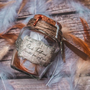 Könnte beinhalten: Ein Glas mit der Aufschrift "Owl Feathers" mit einem Korken, Bindfaden und einem Federanhänger. Das Glas enthält braune Federn und ist von braunen, weißen und grauen Federn auf einer Holzoberfläche umgeben.