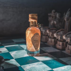 Può includere: Una bottiglia di vetro trasparente piena di liquido dorato scintillante, etichettata "Liquid Luck". La bottiglia ha un sigillo di cera dorata e si trova su una superficie a scacchi blu e bianca, con pezzi degli scacchi sullo sfondo. La bottiglia è alta circa 15 cm.