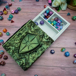 Op de afbeelding: Een groene en gouden decoratieve doos met een schildontwerp. De doos is open en heeft een wit interieur met compartimenten voor dobbelstenen. De doos is omringd door kleurrijke dobbelstenen.