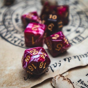 Puede incluir: Cinco dados rojos y blancos con números dorados. Los dados están sobre una superficie marrón con un patrón circular.