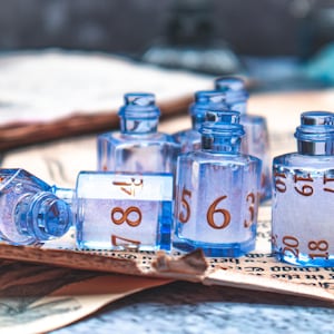 May include: A collection of clear, blue, numbered dice bottles. The bottles are arranged on a vintage paper surface. The numbers are in a warm brown colour. The bottles are designed to resemble dice.