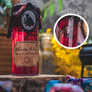 Può includere: Una bottiglia di vetro rosso con l'etichetta "Phantom Phial" e un tappo nero decorativo con un cammeo di corvo. La bottiglia contiene un liquido rosso ed è presentata su una superficie di legno. Include un dado D20.