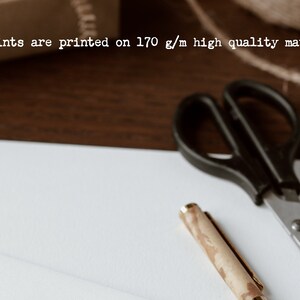K&ouml;nnte beinhalten: Ein wei&szlig;es Blatt Papier mit einer schwarzen Schere und einem Holzstift mit goldener Spitze. Der Text "All my prints are printed on 170 g/m high quality matte paper." ist oben im Bild sichtbar.