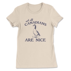 May include: A cream-coloured t-shirt featuring the navy blue text "not all CANADIANS ARE NICE". Below the text is a navy blue illustration of a goose. The t-shirt has a crew neck and short sleeves.