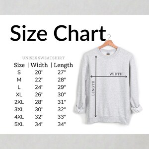 May include: A size chart for a unisex sweatshirt featuring a light grey crewneck sweatshirt on a wooden hanger. The chart lists sizes S through 5XL with corresponding width and length measurements in inches, accompanied by a diagram of the garment.