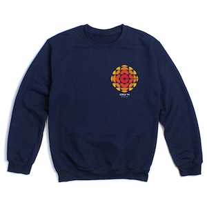 Könnte beinhalten: Ein marineblaues Sweatshirt mit einer Grafik im Vintage-Stil des Logos der Canadian Broadcasting Corporation (CBC). Das Logo ist in Orange-, Gelb- und Rottönen gehalten. Der Text "CIRCA 74" ist unter dem Logo gedruckt.