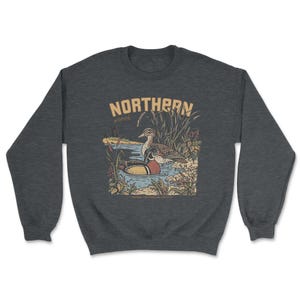 May include: A dark heather gray crewneck sweatshirt featuring a graphic illustration of two ducks swimming in a pond surrounded by reeds and plants. The text NORTHERN is printed in large tan letters above the ducks, with the word march below it.