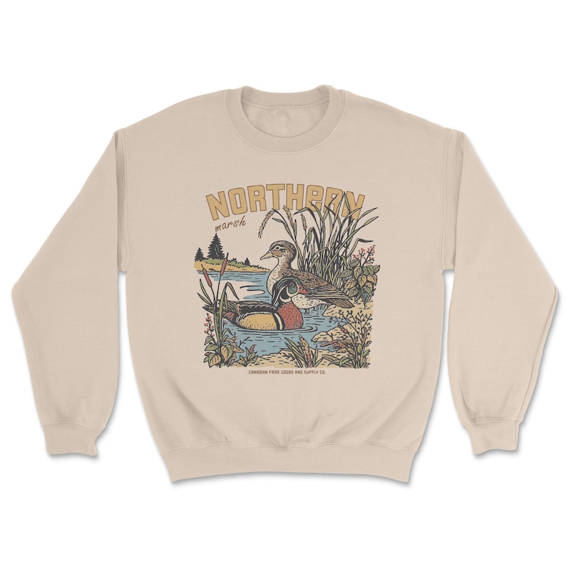 May include: A beige crewneck sweatshirt featuring a graphic illustration of two ducks in a marsh. The text NORTHERN is printed in large letters above the ducks, with marsh below it. Small text at the bottom reads CANADIAN FIBRE GOODS AND SUPPLY CO.