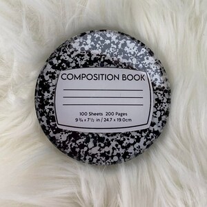 May include: Round composition book with a speckled black and white design. The label reads "COMPOSITION BOOK" with lines for writing. It contains 100 sheets, 200 pages, and measures 9 3/4 x 7 1/2 inches (24.7 x 19.0 cm).
