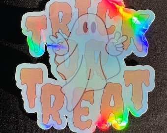 May include: Holographic sticker with a ghost illustration and the words "TRICK TREAT" in a dripping font. The ghost is light blue with a friendly expression, and the text is in a light brown color. The sticker has a rainbow sheen.