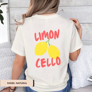K&ouml;nnte beinhalten: Cremefarbenes T-Shirt mit den roten Worten "LIMON CELLO" &uuml;ber zwei gelben Zitronen. Das Shirt hat eine nat&uuml;rliche Farbe und eine lockere Passform. Das Design ist auf der R&uuml;ckseite des Shirts aufgedruckt.