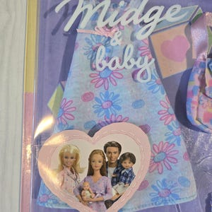 May include: A Midge & baby doll set in its original packaging. The packaging features a light blue dress with pink and blue floral patterns. A heart-shaped image shows a family of dolls. The text "Midge & baby" is visible.