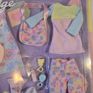 May include: A doll clothing set featuring a pastel color palette. The set includes a dress with blue sleeves and a yellow top, pants, a purse, and baby accessories. The accessories include a bottle, a rattle, and a bear-shaped toy.