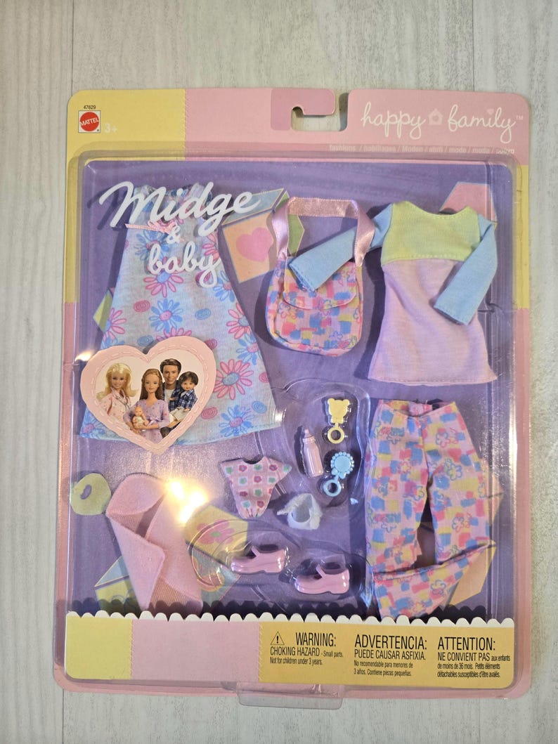 May include: A boxed doll clothing set with the words "Midge & baby" and "happy family". The set includes a dress, purse, top, pants, shoes, and baby accessories. The clothing features floral and heart patterns in pastel colors.