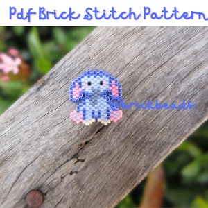 May include: A blue and pink beaded elephant, made with brick stitch, on a wooden surface.