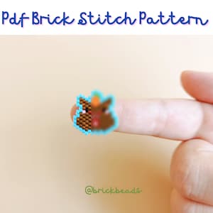 May include: A brown and blue bead pattern of a cartoon character with a white face and a blue hat. The pattern is on a finger.