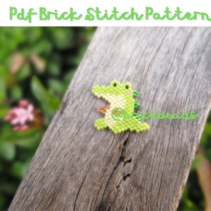 May include: A green and yellow beaded alligator, made with brick stitch, is sitting on a piece of weathered wood. The alligator is facing the right side of the image. The background is blurred and shows green foliage.