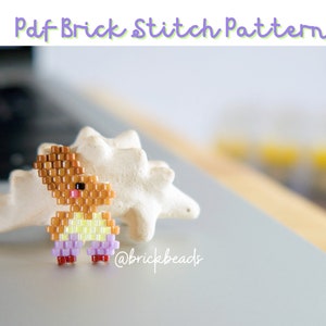 Puede incluir: Un conejito de cuentas marrones y amarillas con pantalones morados y zapatos rojos. El conejito está de pie sobre una concha blanca. La imagen incluye el texto "@brickbeads".