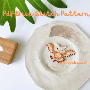May include: A brown and white owl brick stitch pattern, on a white plate with the text "Pdf Brick Stitch Pattern" and "@brickbeads" in orange.