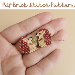 May include: Two small beaded hedgehogs, one brown and one beige, holding a green leaf. The hedgehogs are made with brick stitch beading and are being held in a hand.