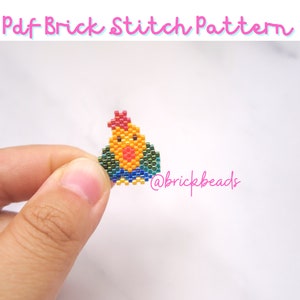 May include: A small, yellow, beaded rooster with a red comb and blue wings. The rooster is being held in a hand against a white background. The text "@brickbeads" is visible in the lower right corner of the image.