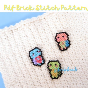 May include: Three small pixel art animal figures made with colorful beads. The figures are a pink and green turtle, a blue and pink bird, and a light green and yellow frog. The figures are on a white knitted surface.