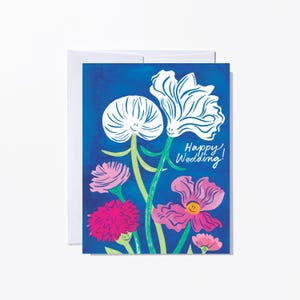 May include: A greeting card with a blue background and a floral illustration. The card features white and pink flowers with green stems. The text "Happy Wedding!" is written in white script. The card is inside a white envelope.