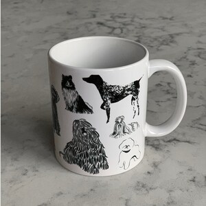 May include: White ceramic mug with black and white illustrations of different dog breeds. The dogs are in various poses, including sitting, standing, and lying down. The mug has a black handle.