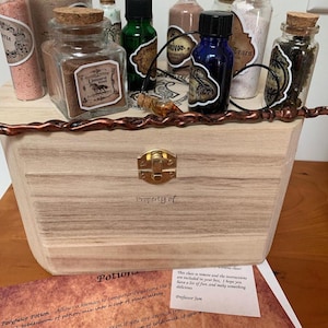 May include: A wooden box with a brass clasp, labeled "Property of," holds various potion bottles with cork stoppers. The bottles contain colorful powders and liquids, with labels like "Unicorn Blood" and "Tears."