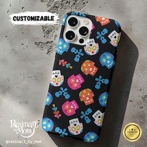 May include: Black phone case with a colorful Day of the Dead sugar skull pattern. The case features a variety of skulls in blue, pink, orange, and white, along with blue crosses and floral accents. The word "CUSTOMIZABLE" is written on the top left.