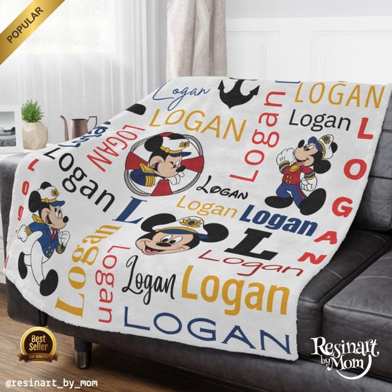 Op de afbeelding: Witte fleece deken met een nautisch thema met Mickey Mouse in een matrozenpak. De deken is versierd met de naam "Logan" die in verschillende kleuren en maten wordt herhaald.