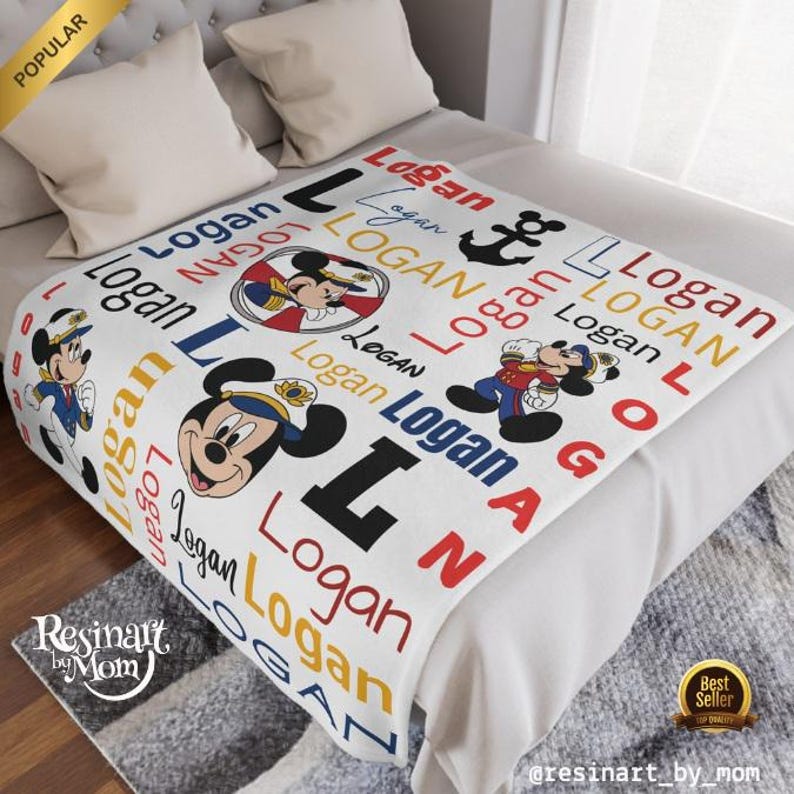 Op de afbeelding: Een wit fleece deken met een nautisch thema met Mickey Mouse. Het deken is gepersonaliseerd met de naam "Logan" die door het hele ontwerp heen wordt herhaald. Het deken heeft een rood-wit-blauw kleurenschema met een anker en Mickey Mouse in een matrozenpak.
