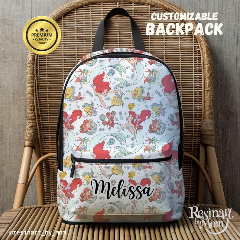 Puede incluir: Mochila blanca con un patr&oacute;n colorido de Ariel la Sirenita, conchas marinas y peces. La mochila tiene una cremallera negra y una correa negra. El nombre "Melissa" est&aacute; escrito en cursiva negra en la parte delantera de la mochila.