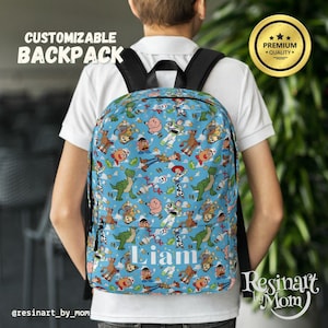 Op de afbeelding: Een blauwe, aanpasbare rugzak met een Toy Story-thema. De rugzak heeft verschillende Toy Story-personages, waaronder Woody, Buzz Lightyear en Jessie. De rugzak heeft een groot vak aan de voorkant met de naam "Liam" in wit.