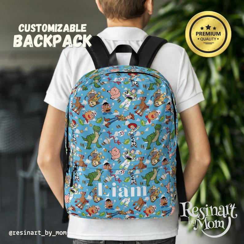 Op de afbeelding: Een blauwe, aanpasbare rugzak met een Toy Story-thema. De rugzak heeft verschillende Toy Story-personages, waaronder Woody, Buzz Lightyear en Jessie. De rugzak heeft een groot vak aan de voorkant met de naam "Liam" in wit.