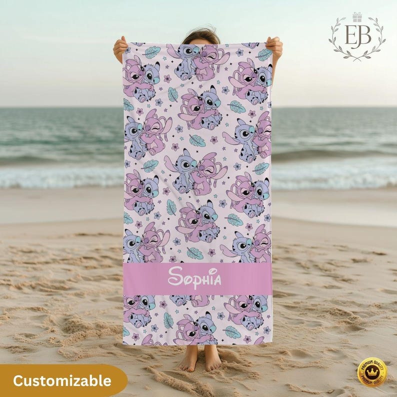 May include: A light pink beach towel featuring a repeating pattern of cartoon characters in shades of blue and pink. A pink band at the bottom displays the name "Sophia" in white script. The word "Customizable" is in a yellow oval at the bottom.
