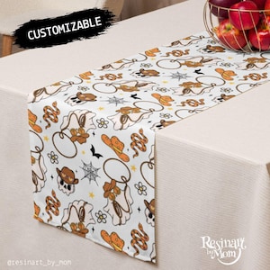May include: White table runner with a repeating pattern of cowboy ghost figures, cowboy hats, snakes, and spiderwebs. The design includes orange, brown, and black elements. The word "CUSTOMIZABLE" is printed on the top left.
