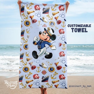May include: A blue beach towel with a nautical theme featuring Mickey Mouse dressed as a captain. The towel has a repeating pattern of anchors, ships, compasses, and Mickey Mouse heads. The text "CUSTOMIZABLE TOWEL" is in the upper right corner of the towel.
