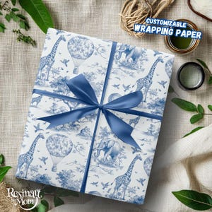 Könnte beinhalten: Weißes Geschenkpapier mit blauem Safari-Design mit Giraffen, Elefanten und Heißluftballons. Ein blaues Satinband ist um das Geschenk gebunden. Der Text "CUSTOMIZABLE WRAPPING PAPER" ist sichtbar. Der Markenname "Resinart by Mom" ist ebenfalls sichtbar.